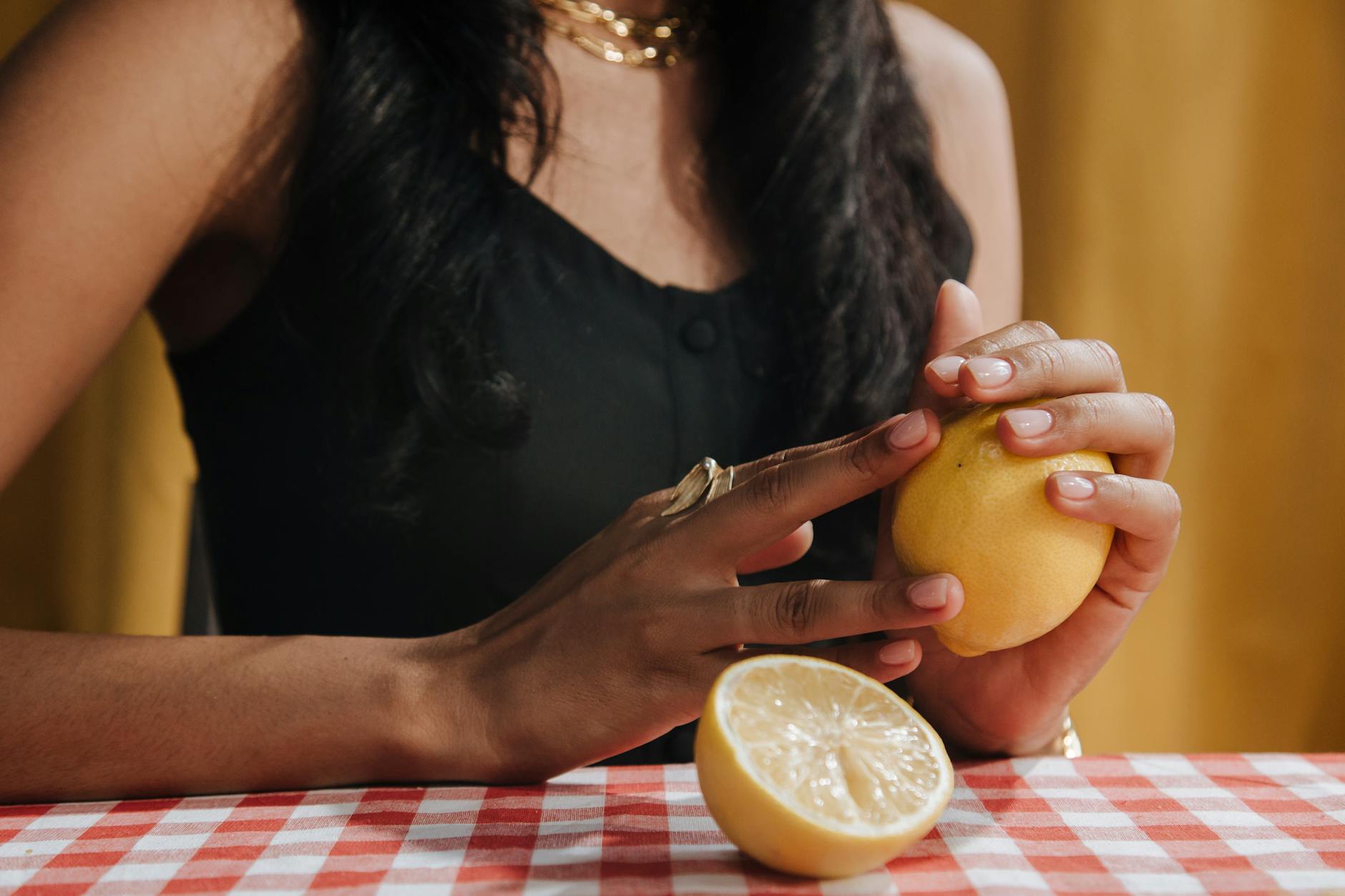 Two hands holding lemon clitoral vibrators against a pastel background